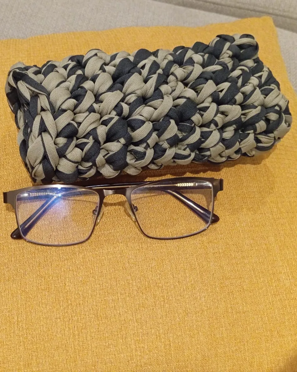 Estuche de crochet para lentes en gris y azul petróleo junto a unos lentes